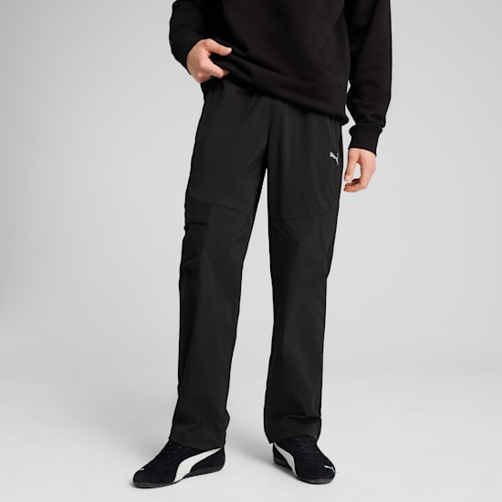 A model poses against a grey backdrop, wearing black trousers and trainers.