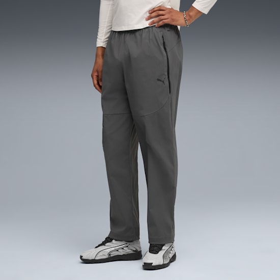 Tegen een grijze achtergrond draagt een model een grijze broek, sneakers en een wit shirt met lange mouwen.