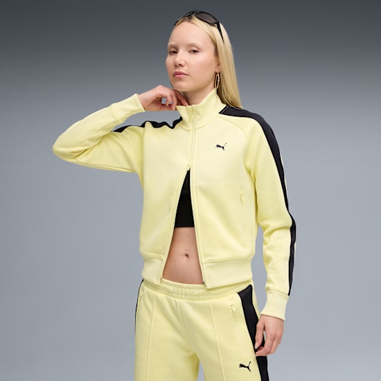 Against a grey backdrop, a model poses in a yellow tracksuit with black accents.
