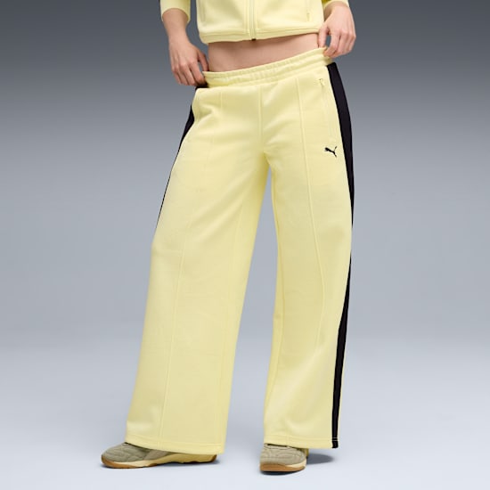 Model poses against grey backdrop, wearing light yellow trousers with a black stripe and trainers.