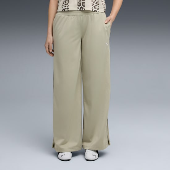 A model poses against grey wearing khaki trousers and white trainers.