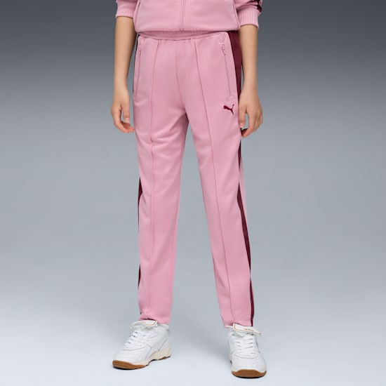 Un modello in piedi su sfondo grigio, indossa pantaloni da tuta rosa e scarpe da ginnastica bianche.