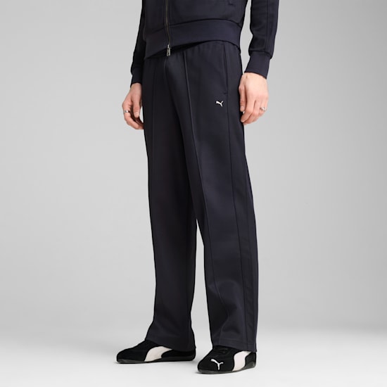 Un modello posa su sfondo grigio, mostrando pantaloni scuri e scarpe da ginnastica bianche e nere.