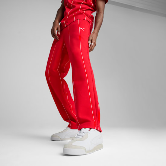 Un modèle pose sur fond gris, portant un pantalon rouge à rayures blanches et des baskets.