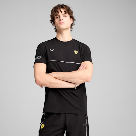 A model with crossed arms poses against a grey backdrop, wearing a black Puma and Ferrari outfit.