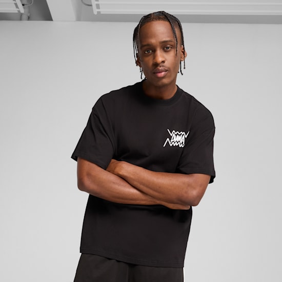 Een model met gekruiste armen poseert tegen een grijze achtergrond, gekleed in een zwart T-shirt.