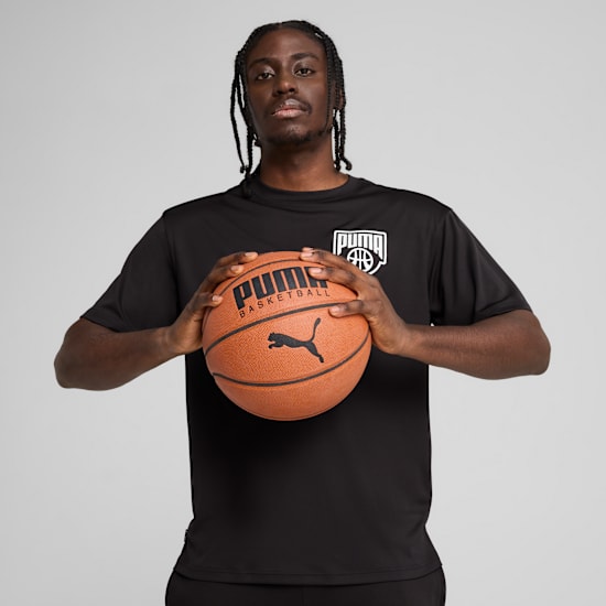 Tegen een grijze achtergrond houdt een model een basketbal vast en draagt een zwart T-shirt.