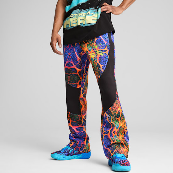 Sur fond gris, un mannequin pose en pantalon à motifs, t-shirt noir et baskets assorties.