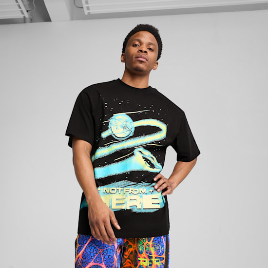 A model poses in front of a grey backdrop, wearing a graphic black t-shirt and patterned shorts.