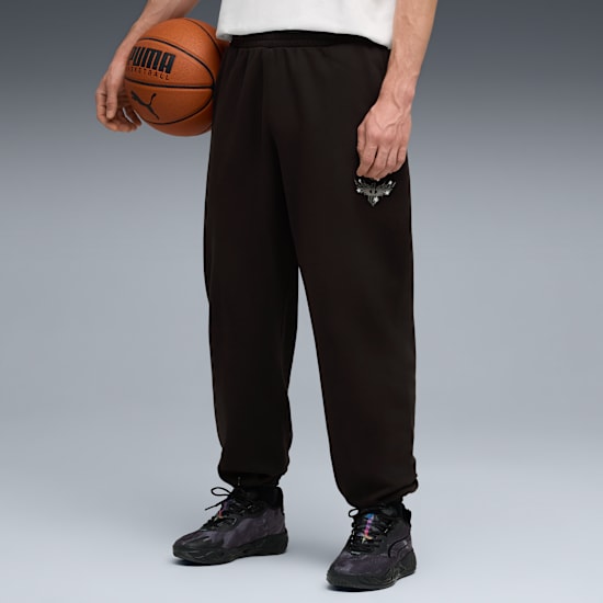 Model on grey holds a basketball, wearing dark joggers and patterned trainers.