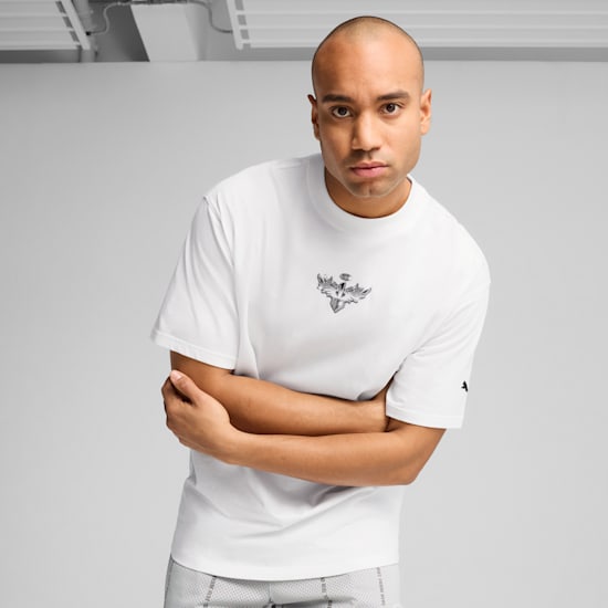 A model with crossed arms poses in front of a grey background wearing a white t-shirt.