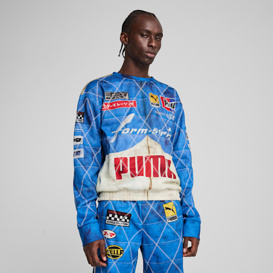 Against a grey backdrop, a model poses wearing a blue, logo-emblazoned tracksuit.
