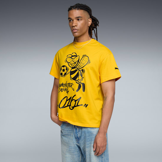 Un modello indossa una t-shirt grafica gialla e jeans su uno sfondo grigio.