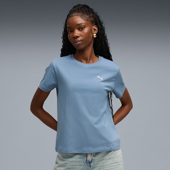 Against grey, a model poses in a light blue t-shirt and denim bottoms.