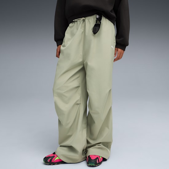 A model poses on grey wearing khaki trousers and colourful trainers.