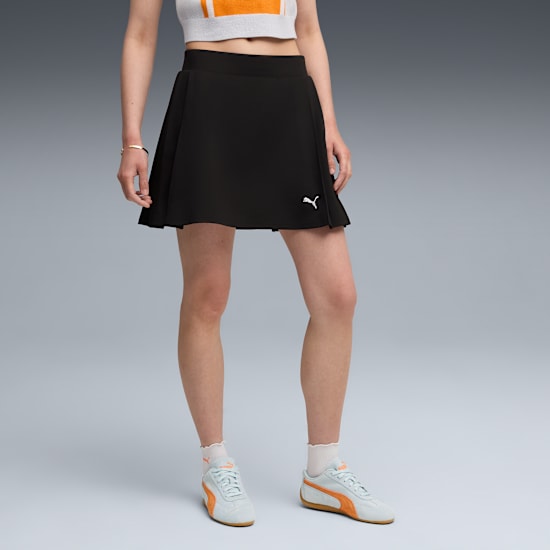 A model poses against a grey backdrop, showcasing a black skirt and light blue trainers.