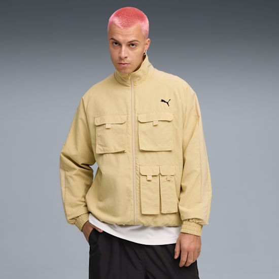 A model with pink hair poses in front of a grey background, wearing a beige jacket.