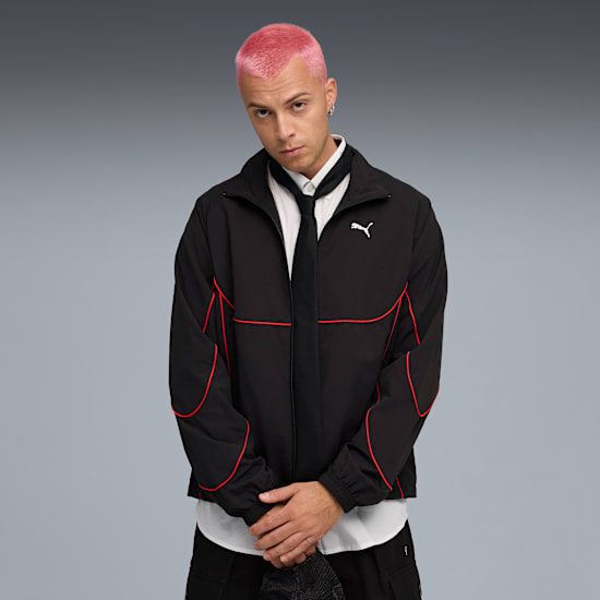 Vor grauem Hintergrund trägt ein Model mit pinken Haaren eine schwarze Jacke mit rotem Rand.