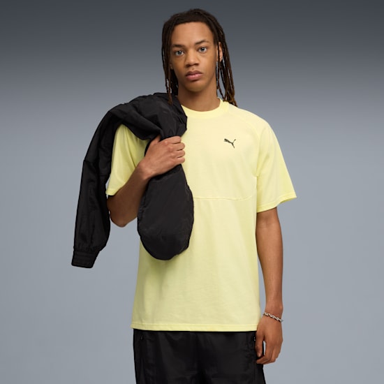 A model with dreadlocks poses against grey, wearing a yellow tee and black shorts.