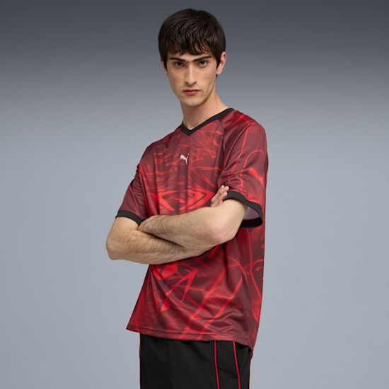 A model with crossed arms wears a patterned red shirt and black shorts on grey.