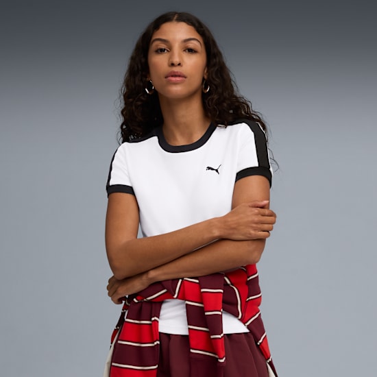 Against grey, a model poses with arms crossed, wearing a white tee and striped top.