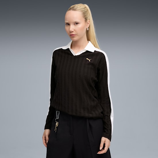 Ein Model posiert vor grauem Hintergrund, mit schwarzem Oberteil und dunkler Hose.