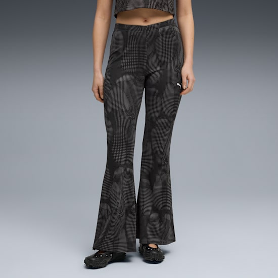 A model poses against grey wearing patterned black flared trousers and dark shoes.