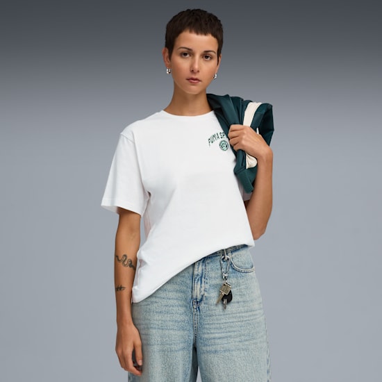 Against a grey backdrop, a model wears a white tee, jeans, and holds a jacket.