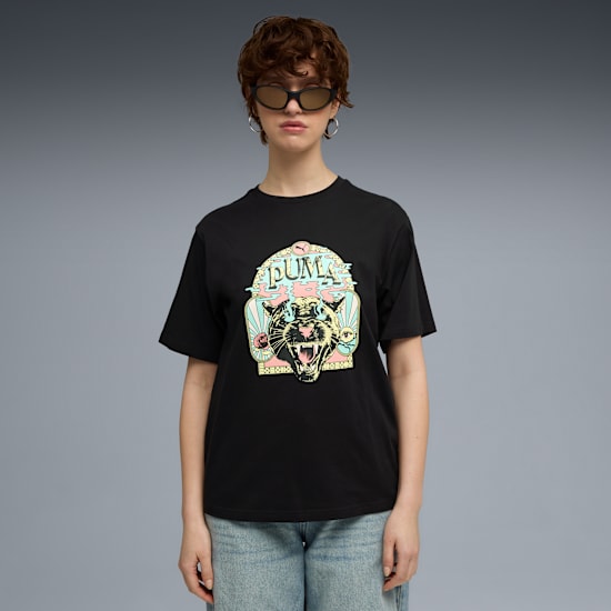 Against a grey backdrop, a model wears sunglasses, a graphic tee, and jeans.