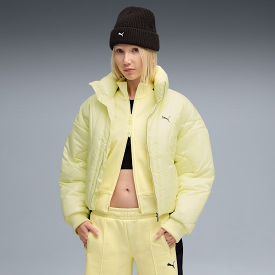 Against grey, a model poses in a black beanie, yellow jacket, top & trousers.