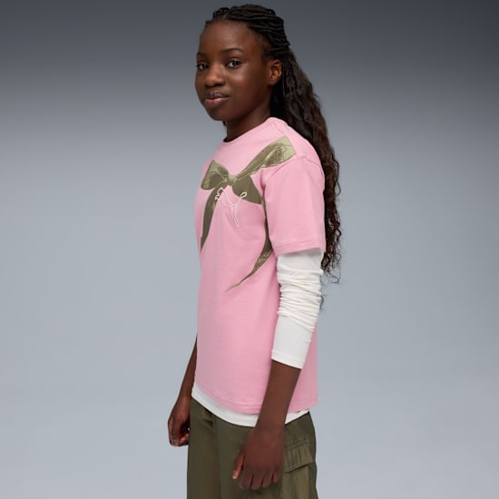 Sur fond gris, un mannequin pose en tee-shirt rose à nœud et pantalon olive.