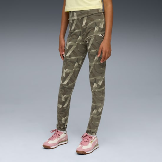 A model is standing against a grey background wearing patterned leggings and pink trainers.