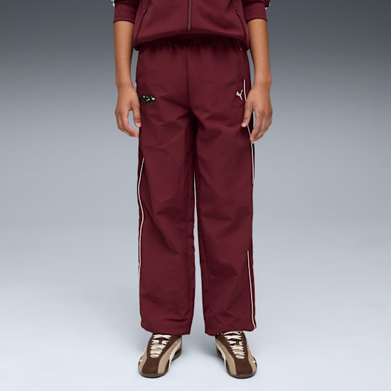 Against grey, a model wears maroon tracksuit bottoms and brown trainers.