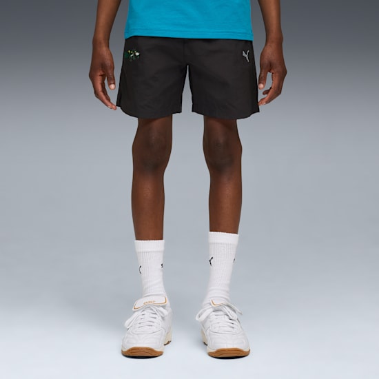 Tegen grijs draagt een model zwarte shorts, blauwe top, witte sokken en sportschoenen.