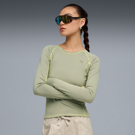 Against grey, a model with arms crossed wears sunglasses, a long-sleeved top, and shorts.