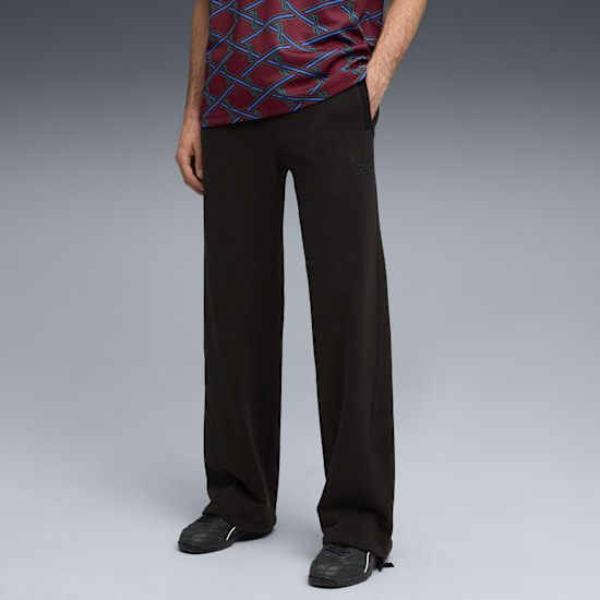 Model poses against grey wearing patterned top, dark trousers, and black trainers.