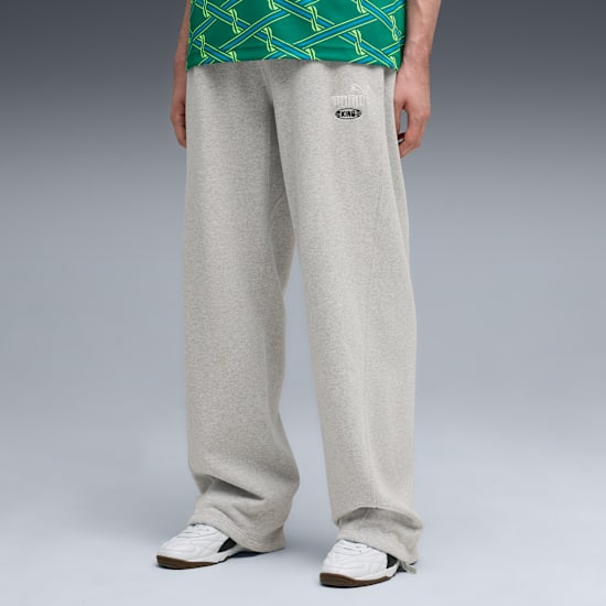 Against grey, a model wears grey sweatpants, a green top, and white trainers.