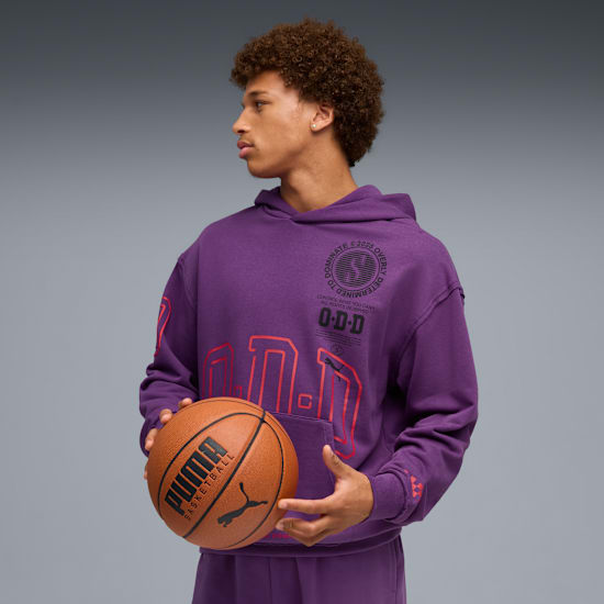 Sur un fond gris, un mannequin tient un ballon de basket et porte un sweat à capuche violet.