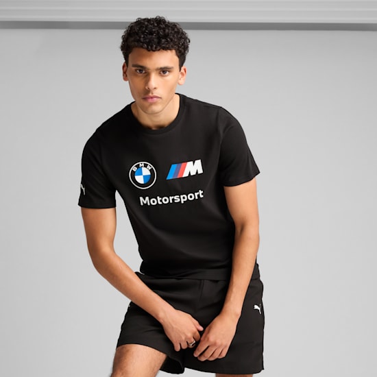 Against a grey backdrop, a model poses in a black BMW Motorsport tee and shorts.