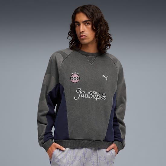 A model poses against grey, wearing a grey sweatshirt with logos and patterned trousers.