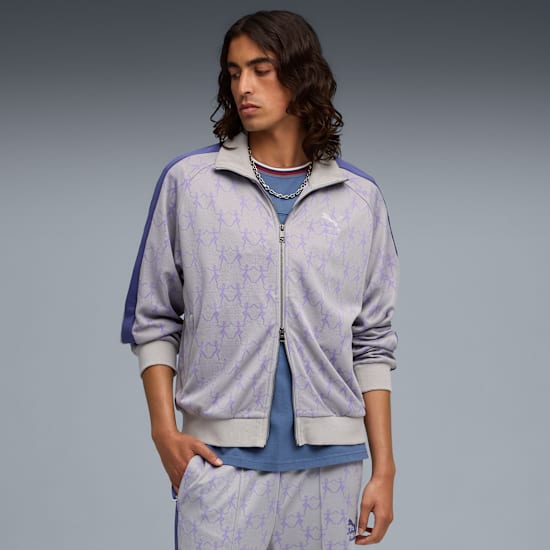 Tegen een grijze achtergrond poseert een model in een jas met ritssluiting en bijpassende broek.