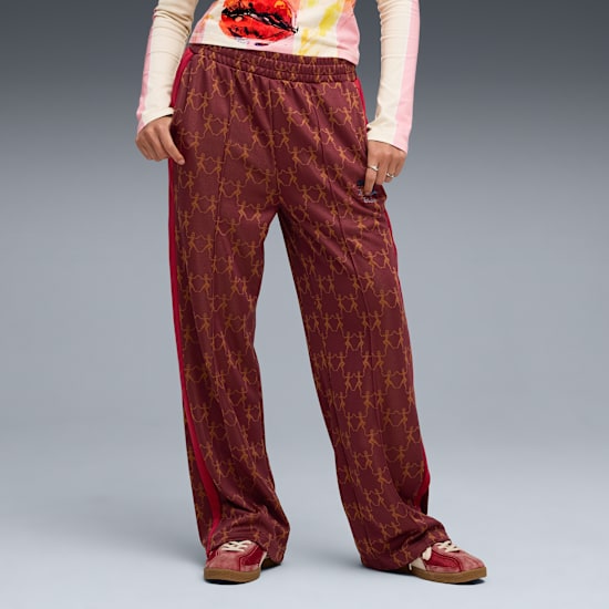 Sur fond gris, un modèle pose, portant un pantalon marron à motifs, un haut et des baskets.