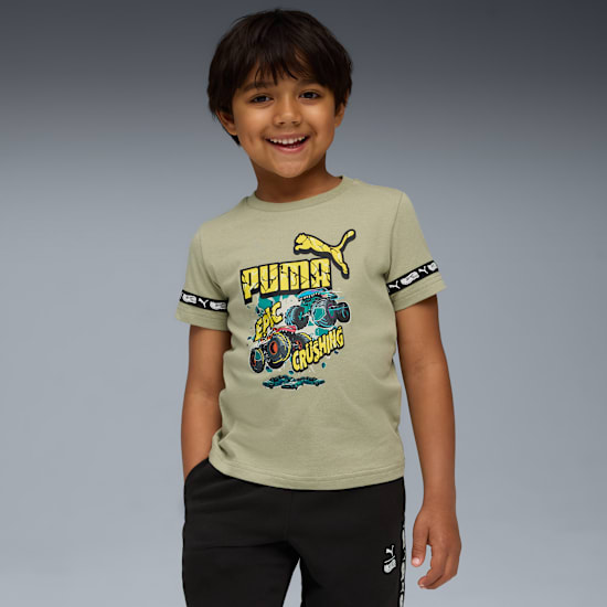 A smiling child poses against a grey backdrop wearing a green t-shirt and black trousers.