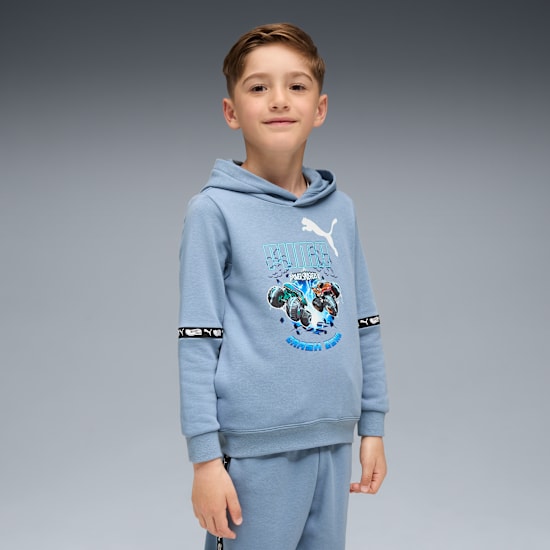 Een kind poseert tegen grijs, draagt een blauwe hoodie en bijpassende joggingbroek.