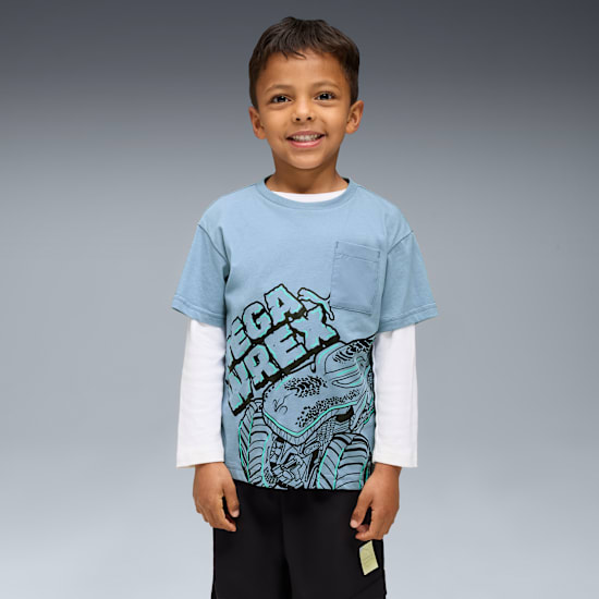 A smiling boy stands against grey, wearing a blue 'Mega Rex' graphic T-shirt and black shorts.
