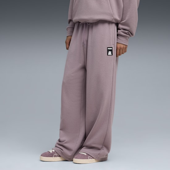 A model stands on a grey background wearing mauve sweatpants and mauve shoes.