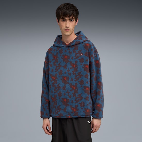 Un modello in posa su sfondo grigio indossa felpa blu fantasia e pantaloncini neri.