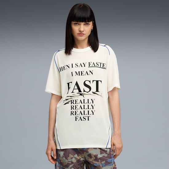 A model stands against grey wearing a slogan t-shirt and patterned shorts.