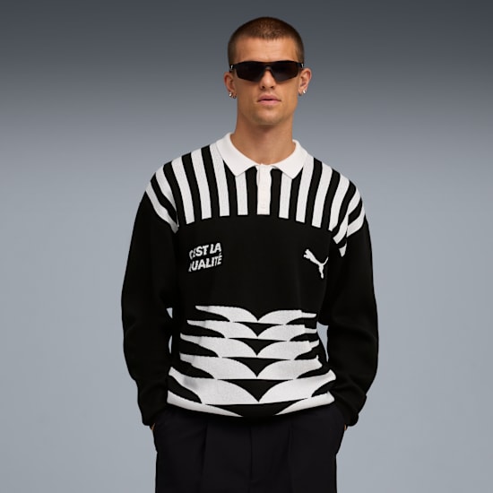 A model poses against grey in a black and white striped polo shirt and dark trousers.