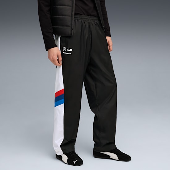 Su sfondo grigio, un modello indossa pantaloni, gilet, top e scarpe Motorsport neri.